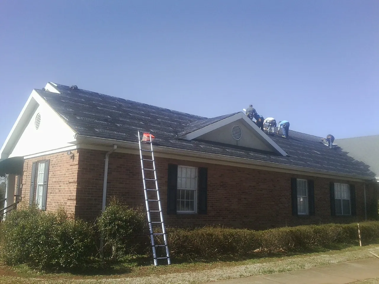 Crew tearing shingles off a brick ranch roof with a ladder set — Metal Roof Repair work by our crew in Lake Hopatcong