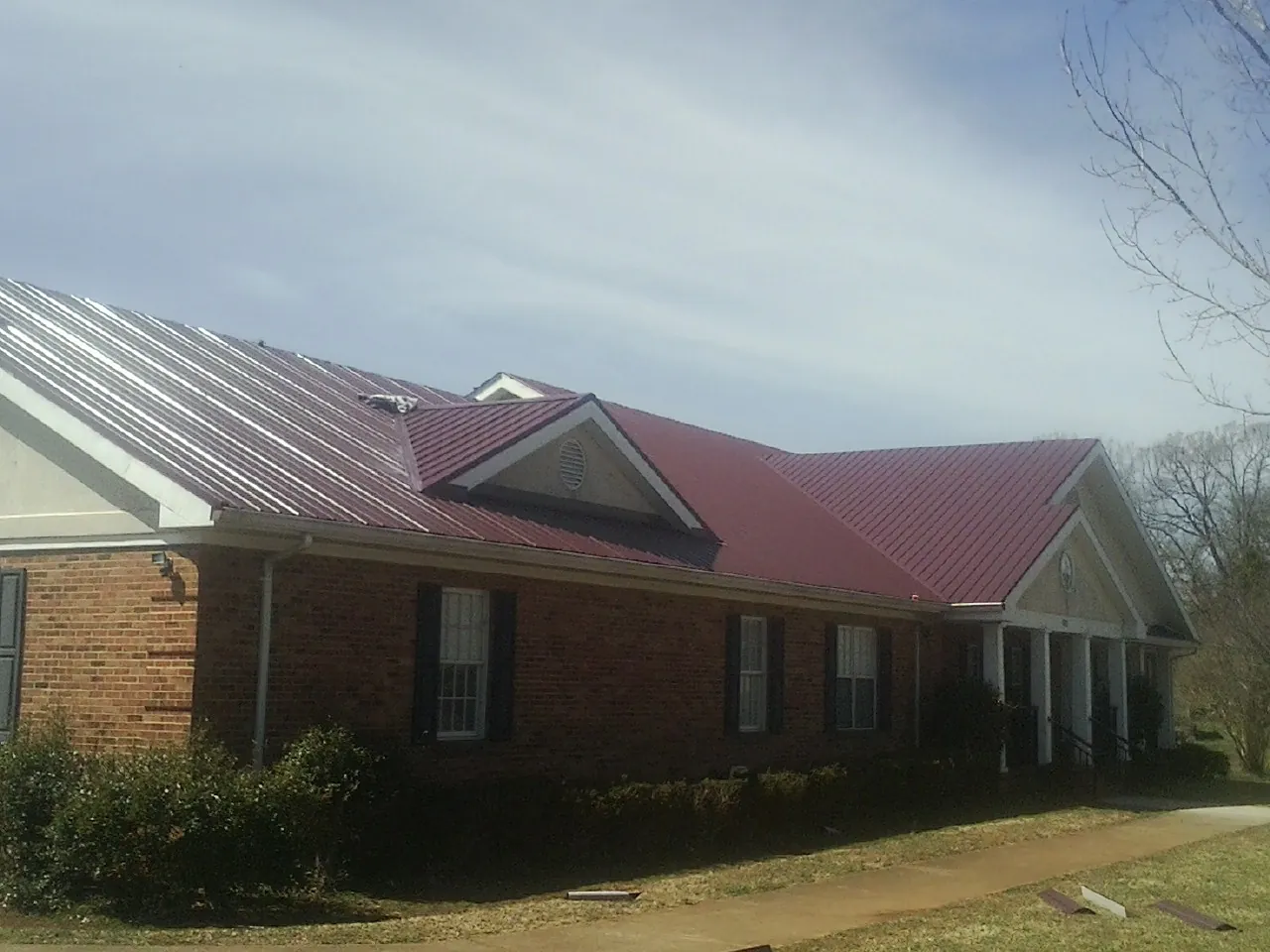 Red metal roof with gabled entries on a long brick building, from a Hail Damage Roof Repair job in Lake Hopatcong