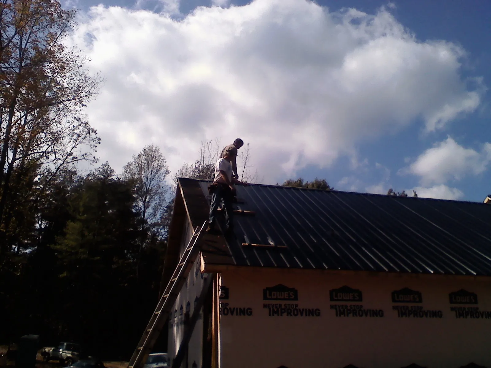 Roofer fastening dark metal panels high against a cloudy sky, from a Roof Inspection job in Lake Hopatcong