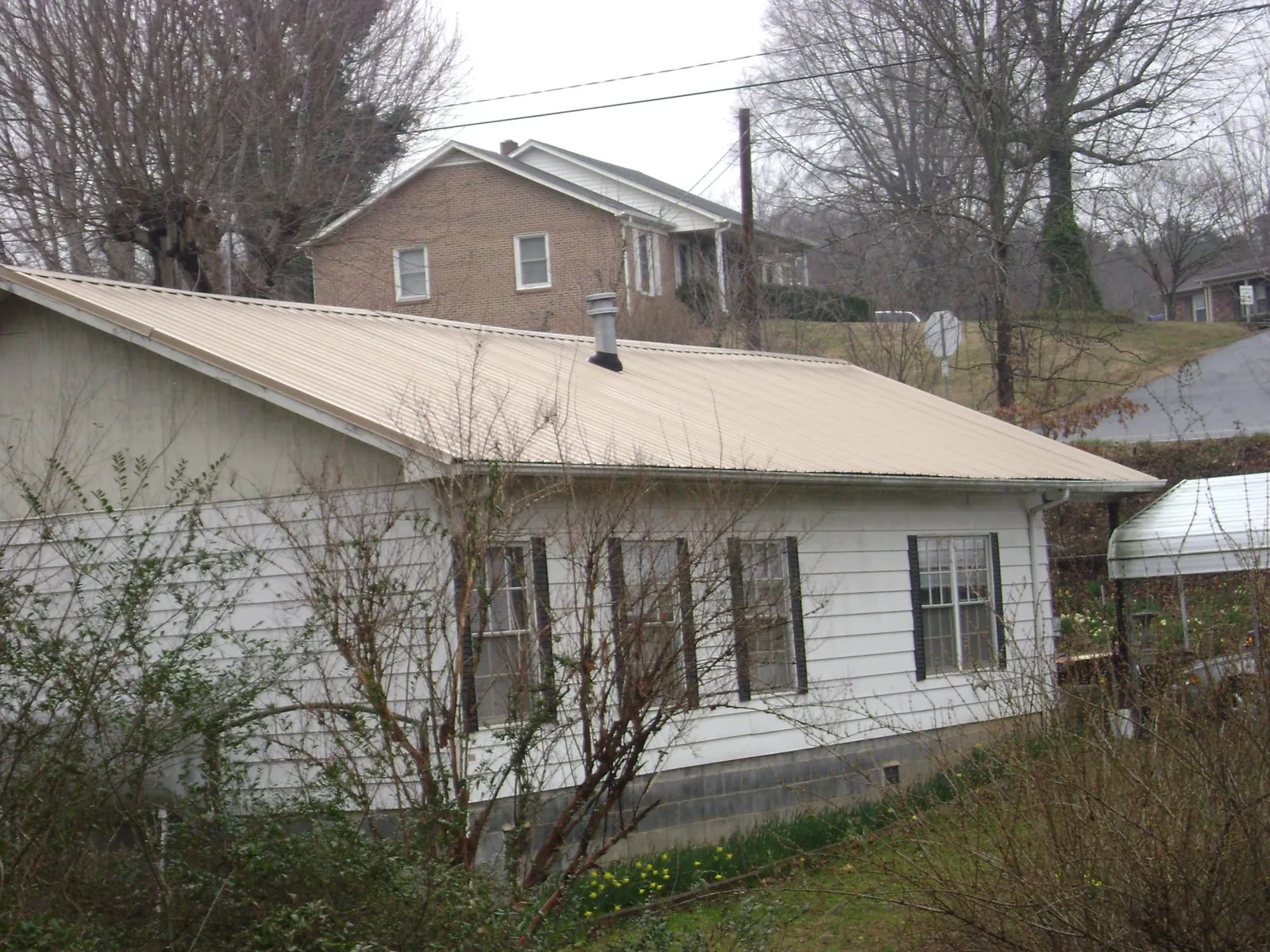 Tan metal roof on a white sided house set into a hillside — Commercial Roofing by Roofing Brothers in Lake Hopatcong